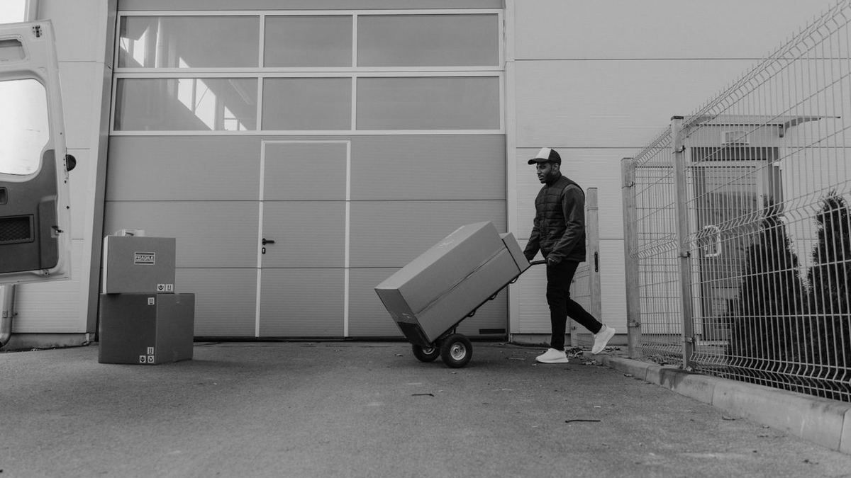 Warehouse worker moving boxes with a hand truck near a delivery van