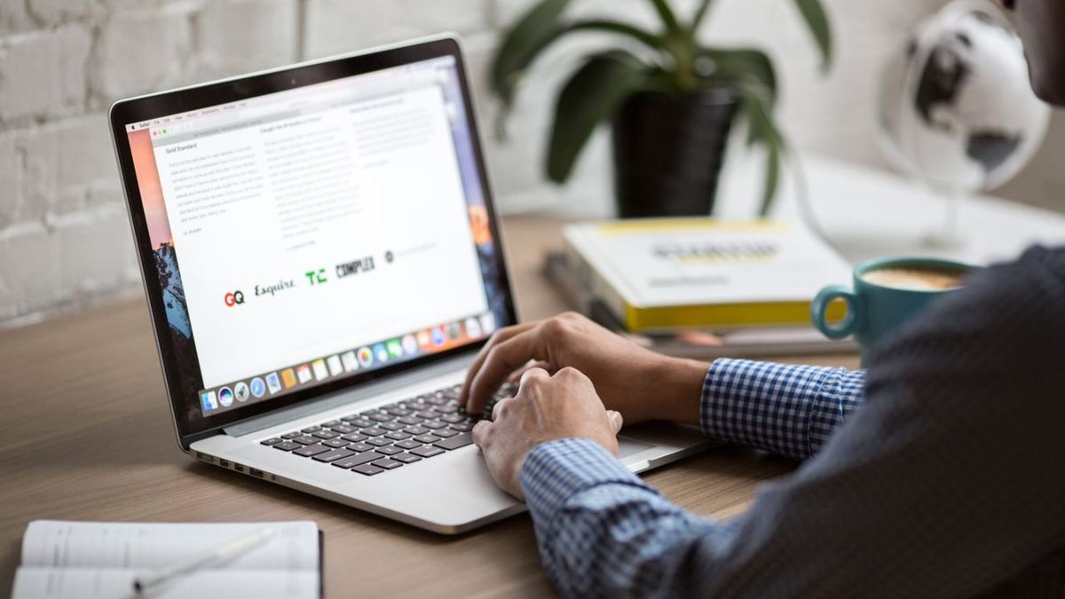 Person typing on a laptop displaying media publication logos