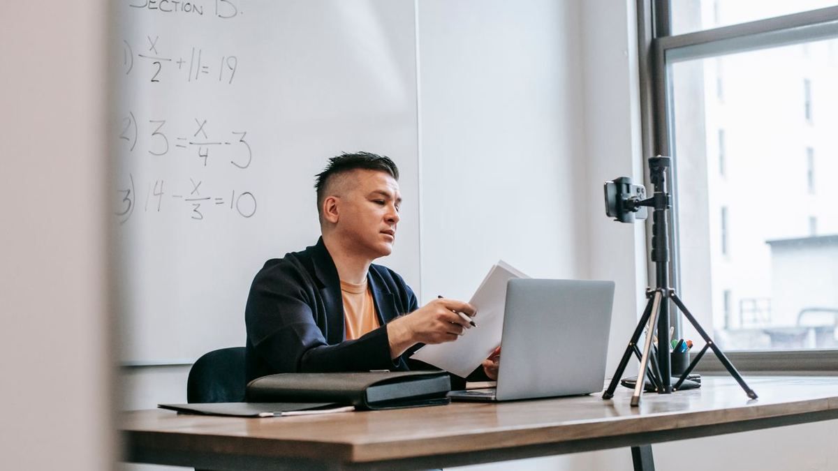 Instructor reviewing notes at a desk with a camera set up to record
