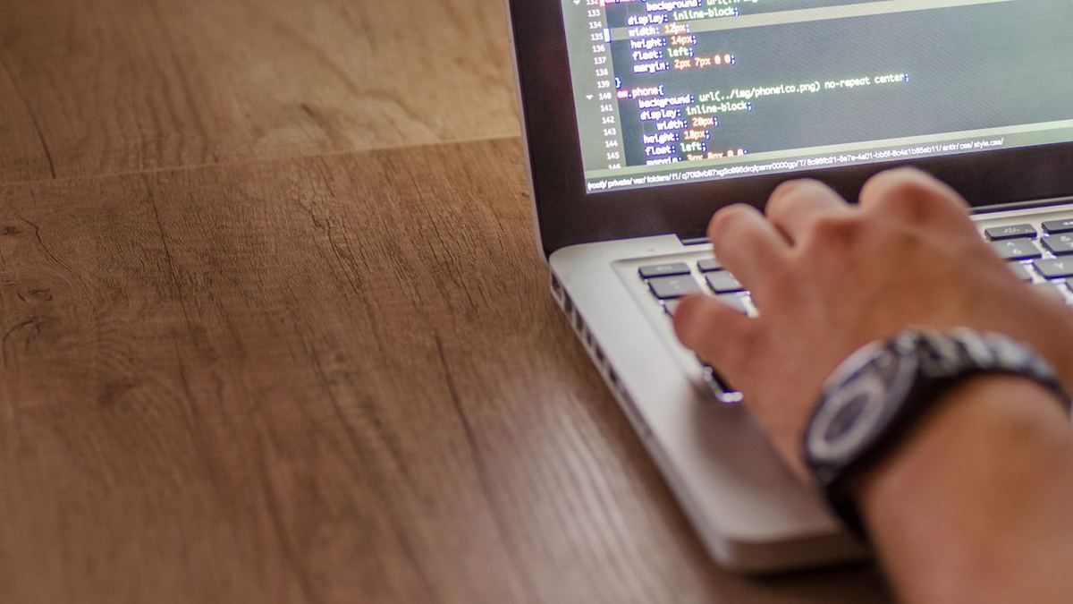 Hand typing website code on a laptop keyboard